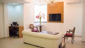 A modern living room with a white sofa, a small round table, a TV mounted on the wall, and a chandelier. - Lis Hotel (Teresina)