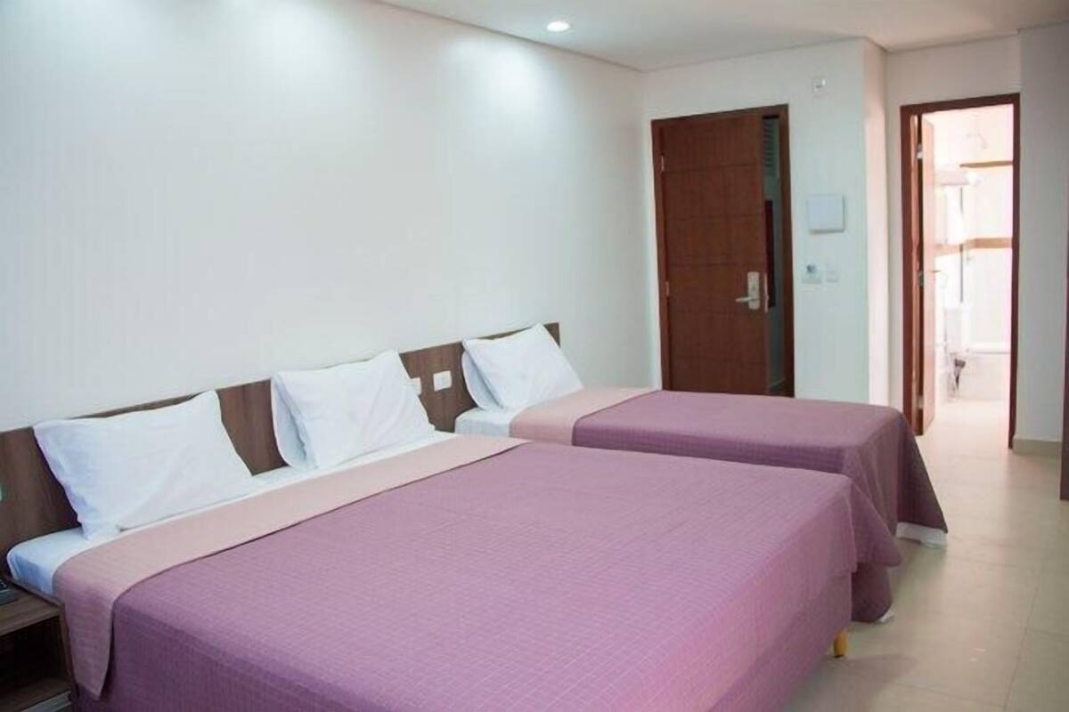 A hotel room with two beds, a wooden door, and a visible bathroom.