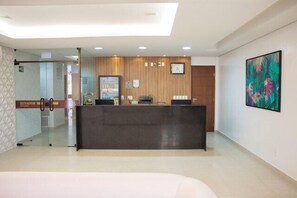 A reception area with a dark reception desk, a clock, and a framed abstract painting on the wall. - Lis Hotel (Teresina)