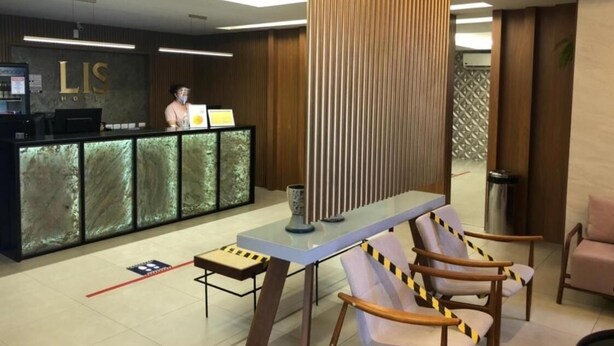 A reception area with a modern desk, a receptionist, and a seating area with chairs. - Lis Hotel (Teresina)