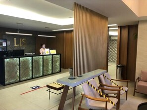 Un área de recepción con un mostrador moderno, una recepcionista y una zona de estar con sillones.