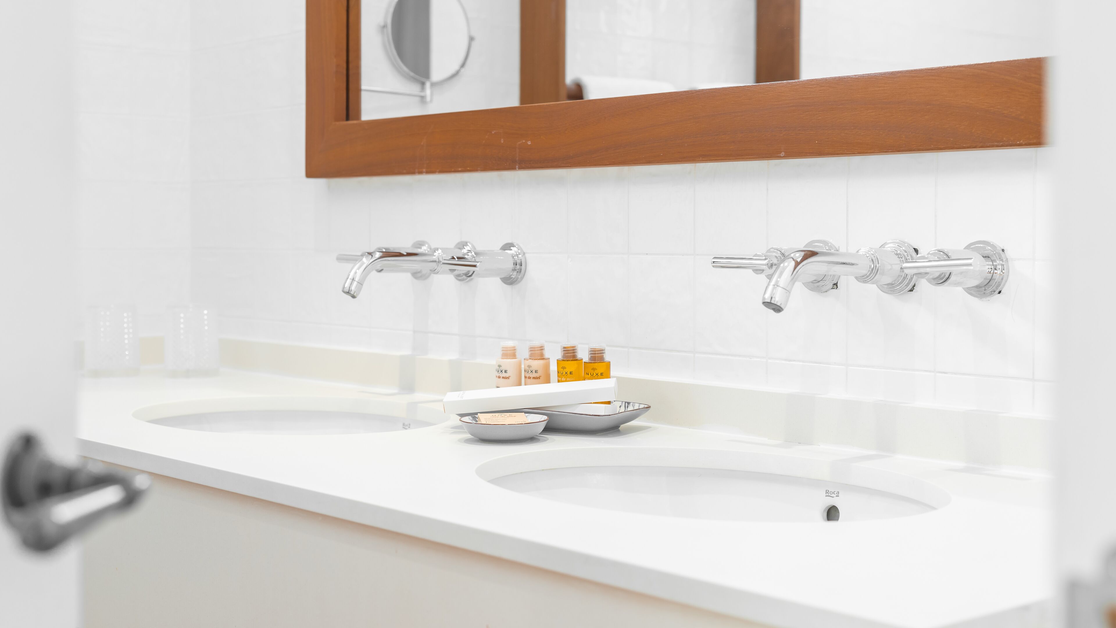 A bathroom with two sinks, a mirror, and a shelf with toiletries.