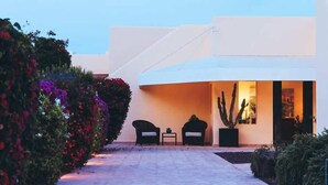 Un bâtiment moderne à la façade blanche, doté d’un espace extérieur abrité avec deux chaises, et d’un cactus dans un pot.