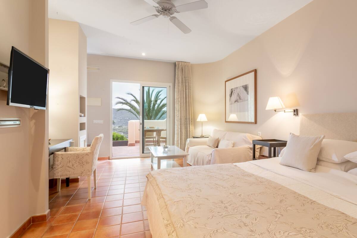 Een hotelkamer met een bed, een televisie, een bureau, een stoel, een tafel, een lamp en uitzicht op de omgeving.