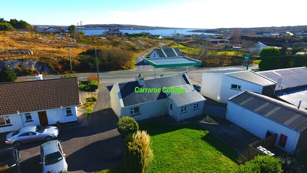 Ein Wohngebiet mit Häusern, darunter das Carraroe Cottage, mit einem gepflasterten Einfahrt und einer Rasenfläche.