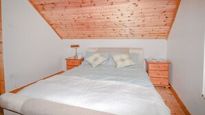 Ein Schlafzimmer mit geneigtem Holzboden, einem Bett mit weißer Bettwäsche, zwei Nachttischen und einem Beistelltisch.