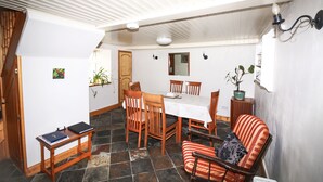 Ein Essbereich mit Tisch und Stühlen, ein kleiner Holztisch mit Büchern und ein gestreifter Sessel.