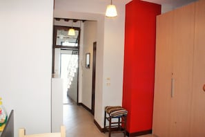 A hallway with a red accent wall, a wooden wardrobe, and a chair with a striped cushion.