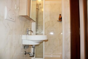 A bathroom with a white sink, a glass-enclosed shower, and a wooden door. - Mario Apartment 5012 (Venice)