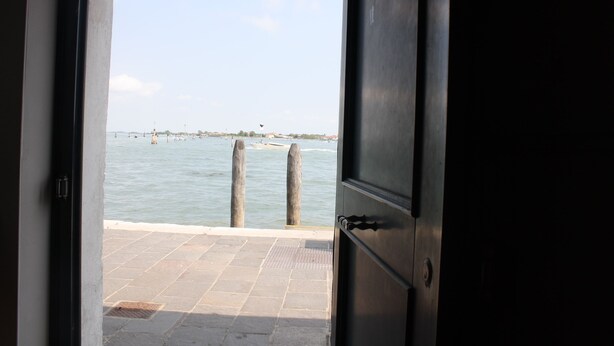 A view from inside a building looking out to a body of water with a dock and bollards. - Mario Apartment 5012 (Venice)