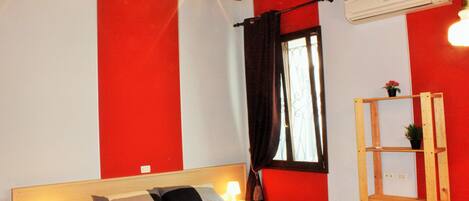 A bedroom with a bed, bedside lamps, a window with curtains, an air conditioning unit, and a wooden shelf.