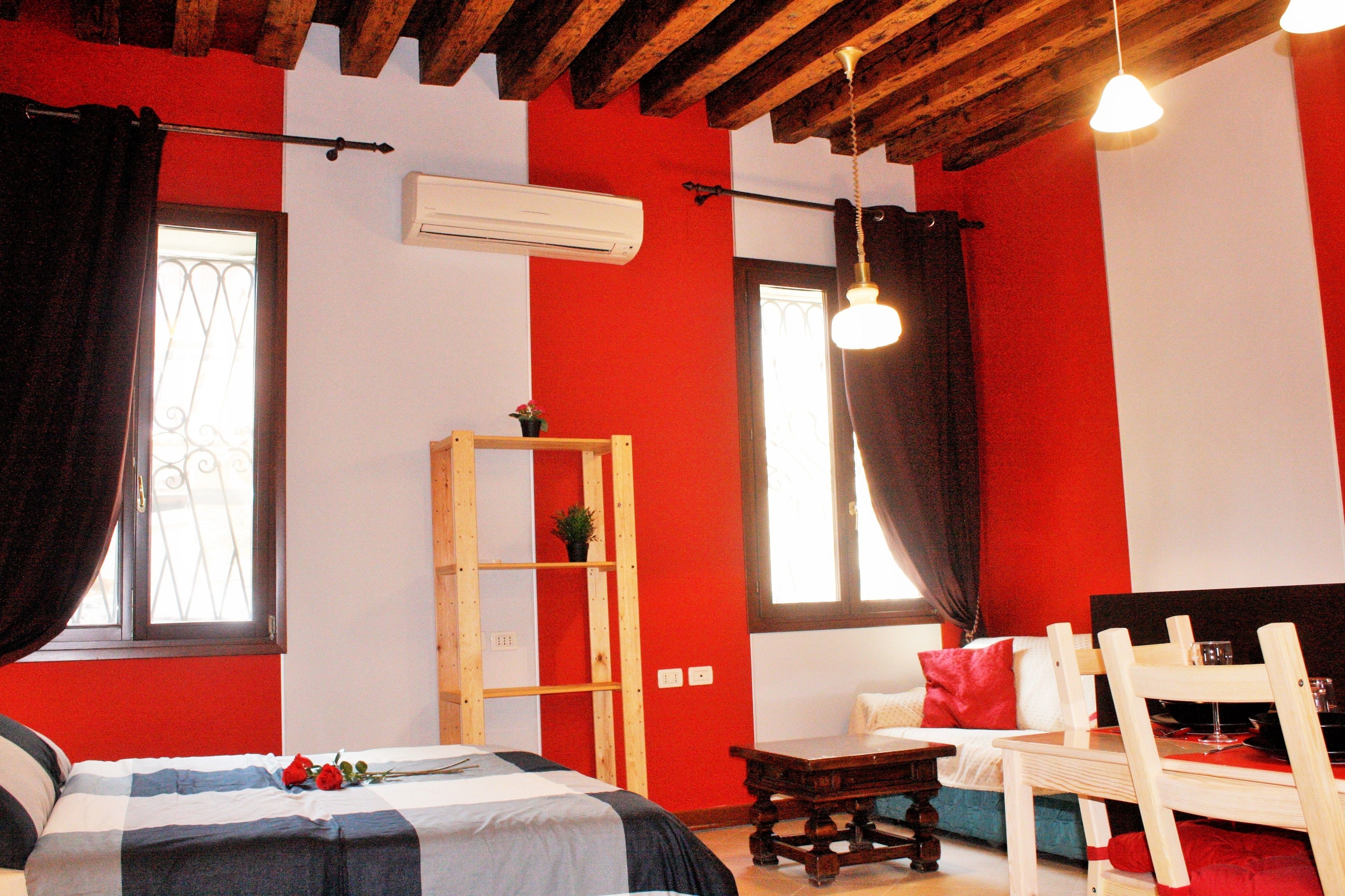 A room with a bed, a wooden table, a sofa, and a window with curtains.