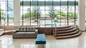 Un vestíbulo moderno con un sofá gris, un otoman azul y una escalera que lleva a un área exterior con piscina.