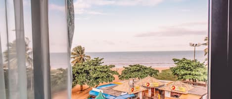 Vista costera desde una ventana con vista a una playa con tiendas pequeñas y palmeras.