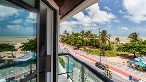 Vista desde un balcón sobre una playa con palmeras y una carretera con coches.