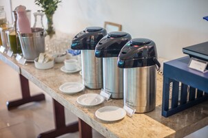 A kitchen counter with stainless steel thermos cups, a few plates, and a blue cabinet.