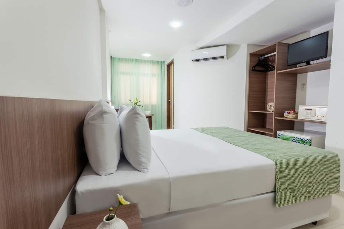 Una habitación de hotel moderna con cama, televisor, armario y una pequeña mesa con un florero.