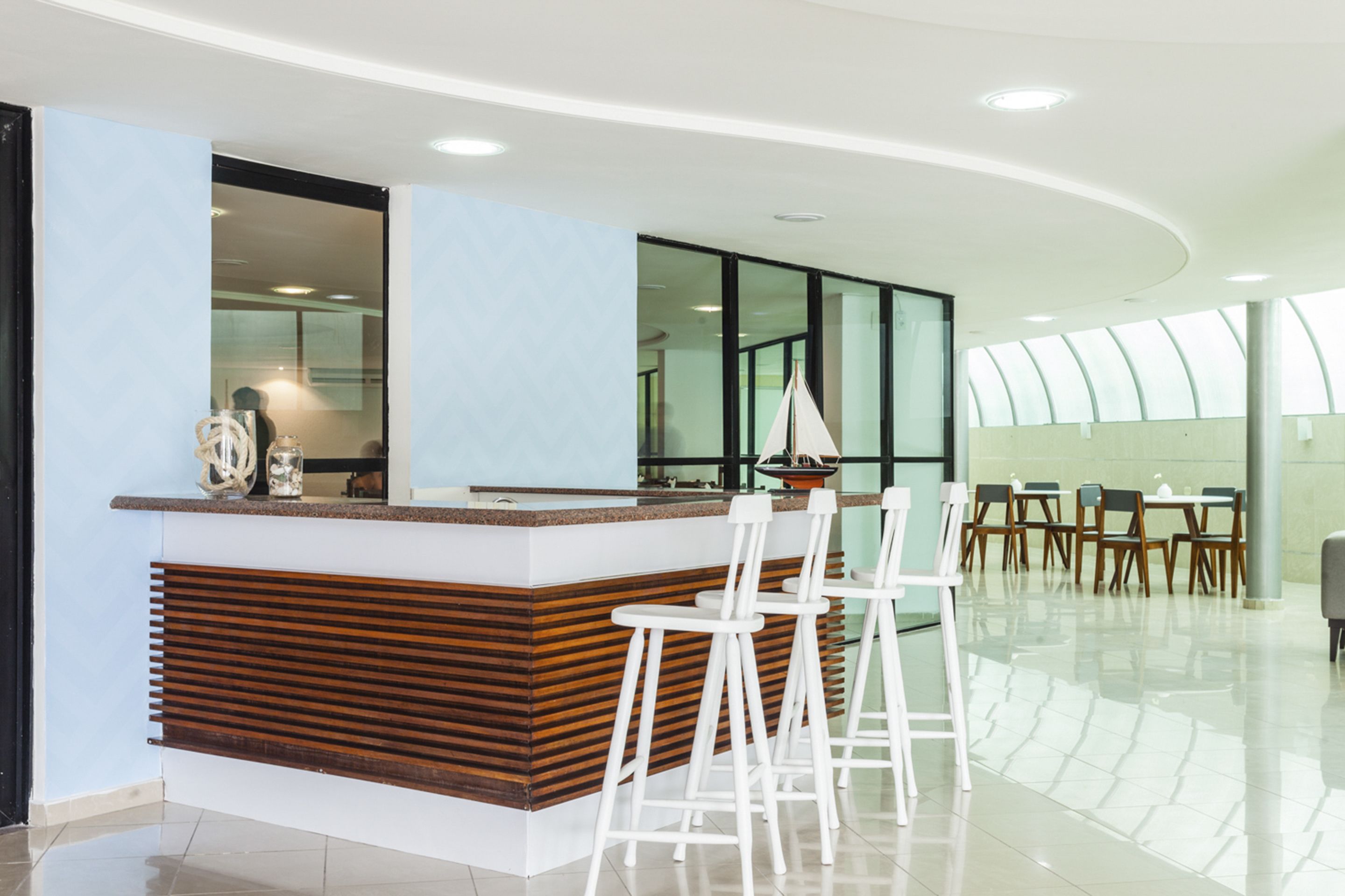 A modern bar area with a wooden counter and white bar stools.