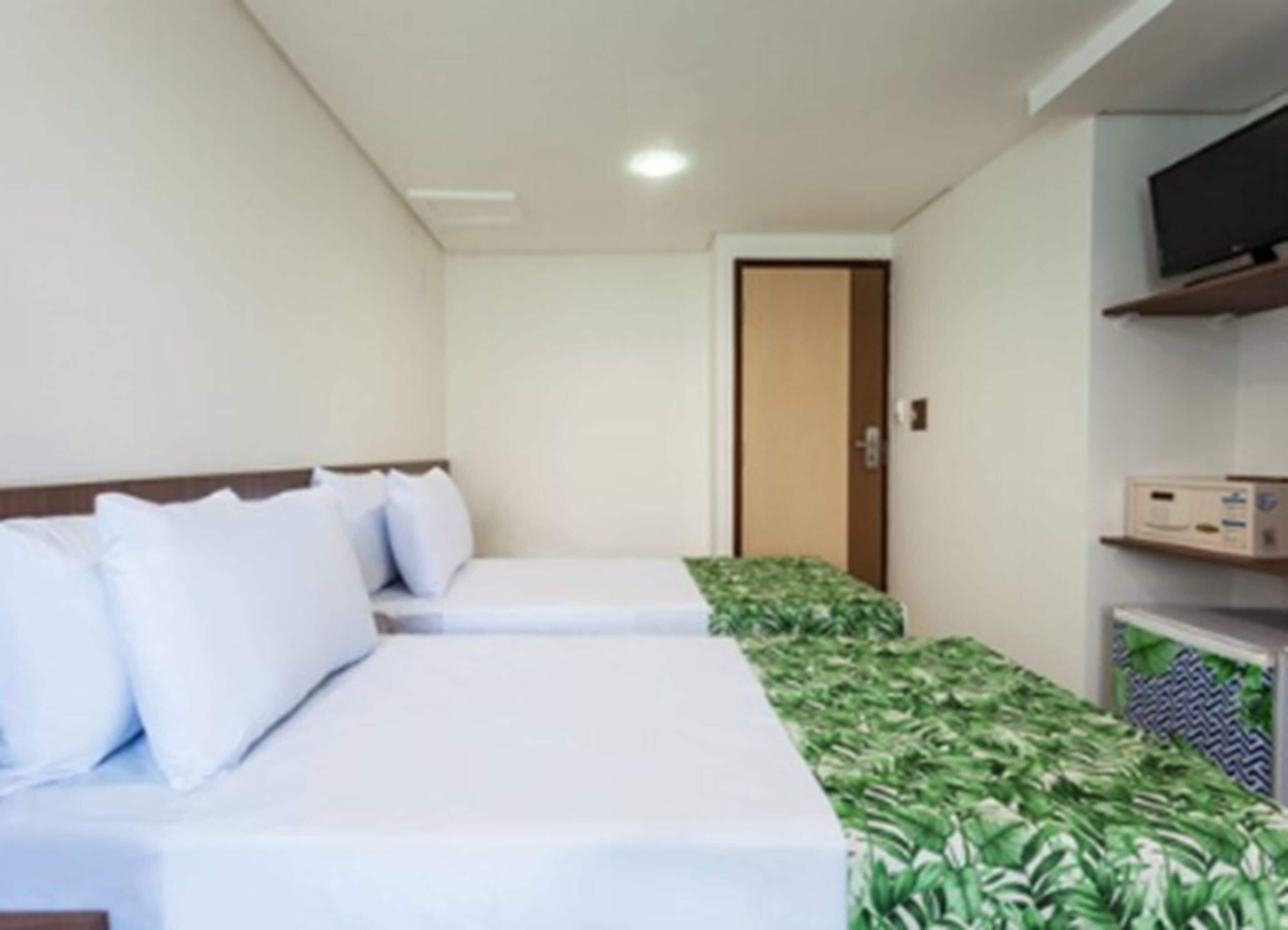 Une chambre d’hôtel avec deux lits simples, un téléviseur posé sur une étagère et une porte visible au fond.