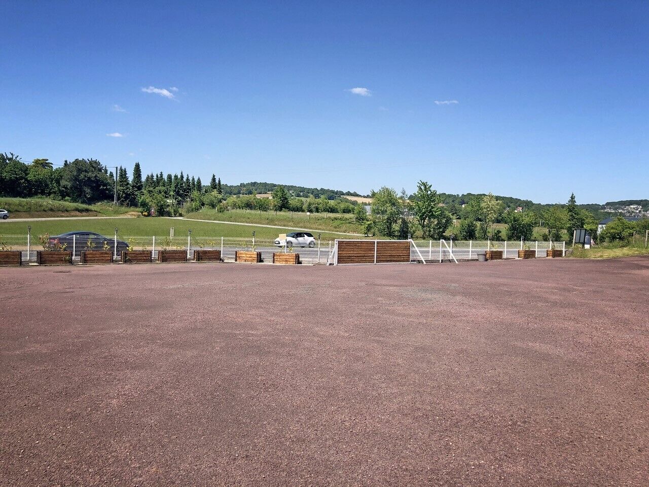 Una arena ecuestre al aire libre con suelo de grava, rodeada de vallas y árboles.