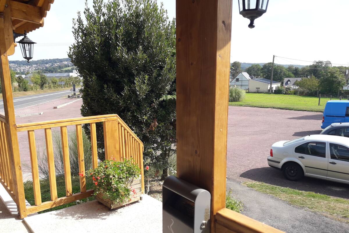 Un balcon en bois donnant sur une rue résidentielle, une voiture garée et un grand arbre.
