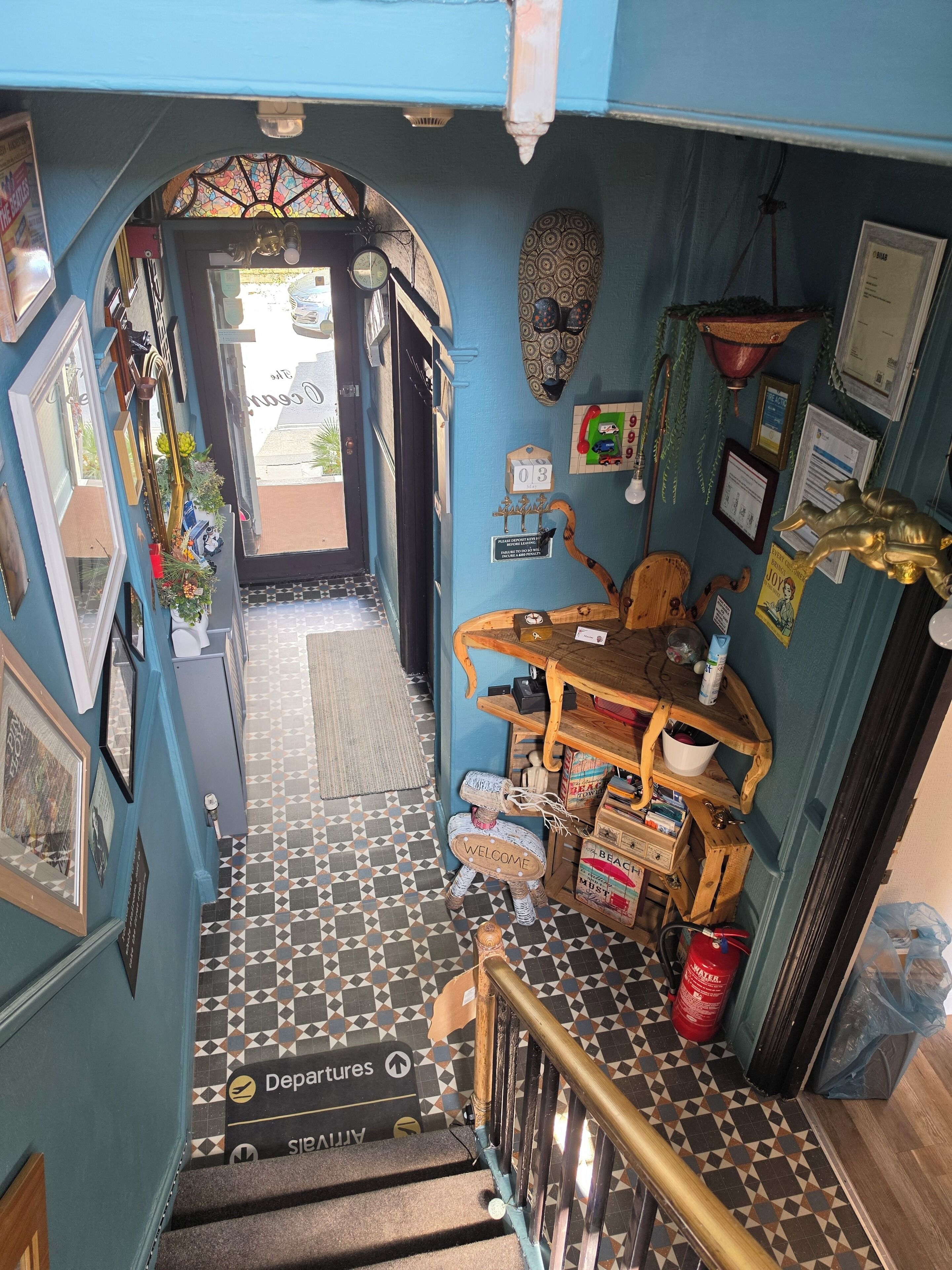 A staircase with a patterned floor leading to a door, a welcome sign, and various items on shelves and the wall.