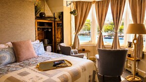 A hotel room with a bed, a chair, a desk, a lamp, and a view of the water. - The Ocean Guesthouse (Weymouth)