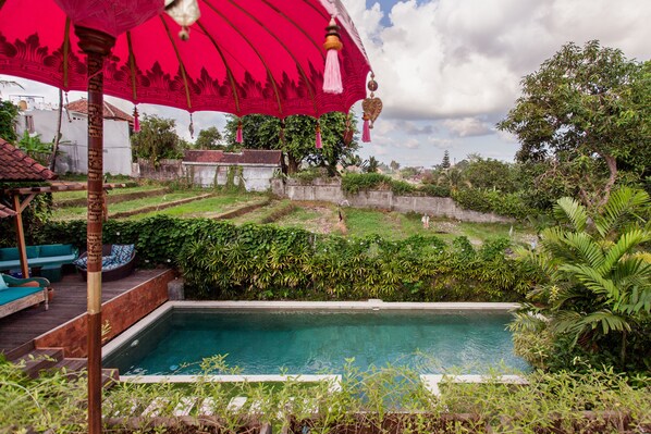A swimming pool with a wooden deck and a red umbrella.
