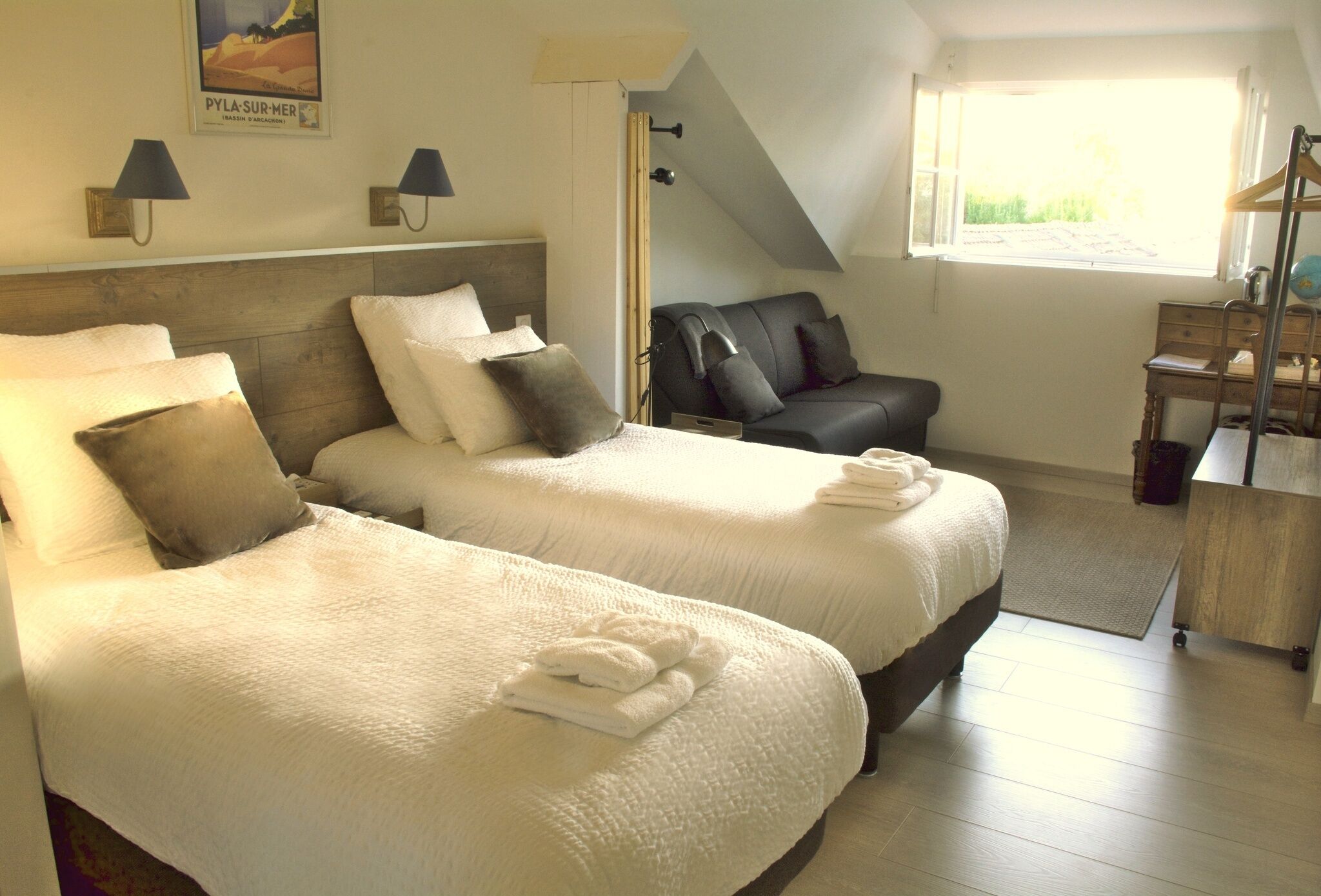 A hotel room with two beds, a desk, a chair, and a window with a view.
