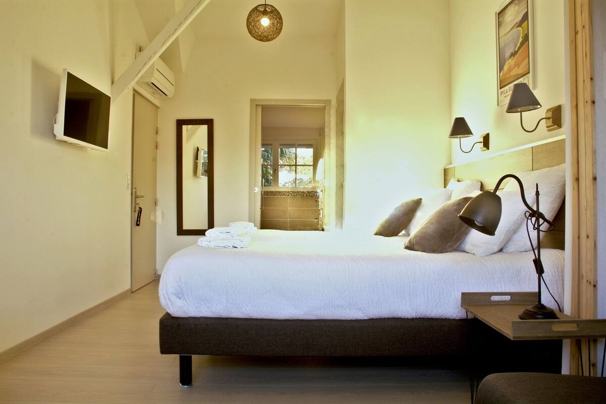 A hotel room with a large bed, bedside lamps, a flat-screen TV, and a view of the outdoors through a door.