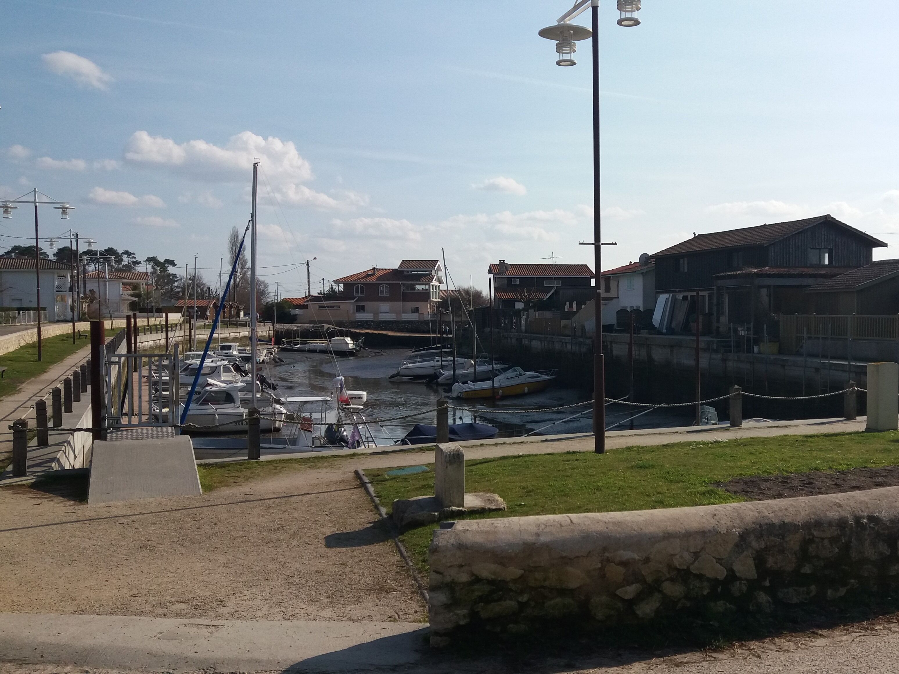 A marina with boats docked, a stone wall, and buildings in the background.