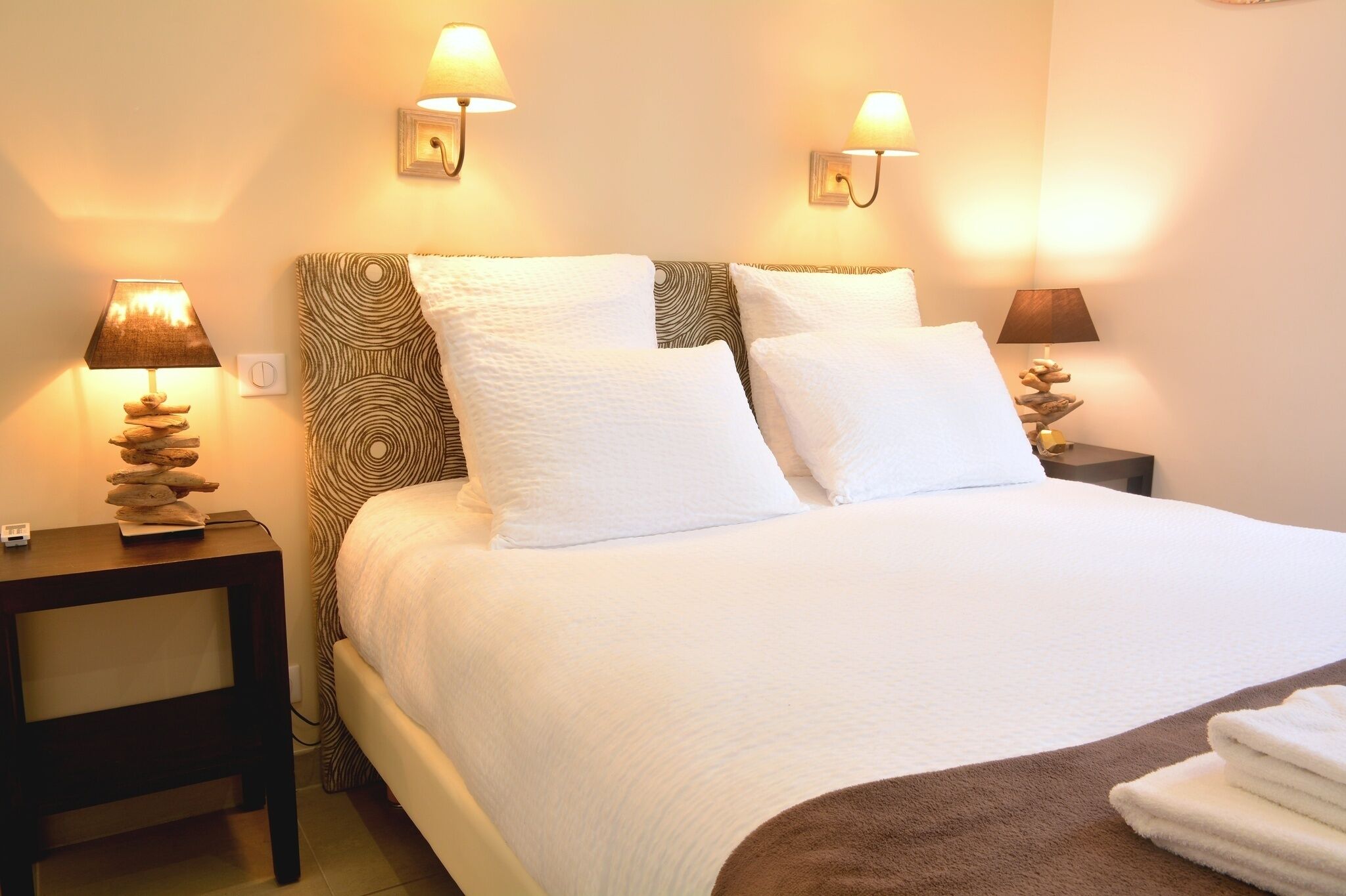Cama bem arrumada com lençóis brancos, duas luminárias de cabeceira e cabeceira estampada.
