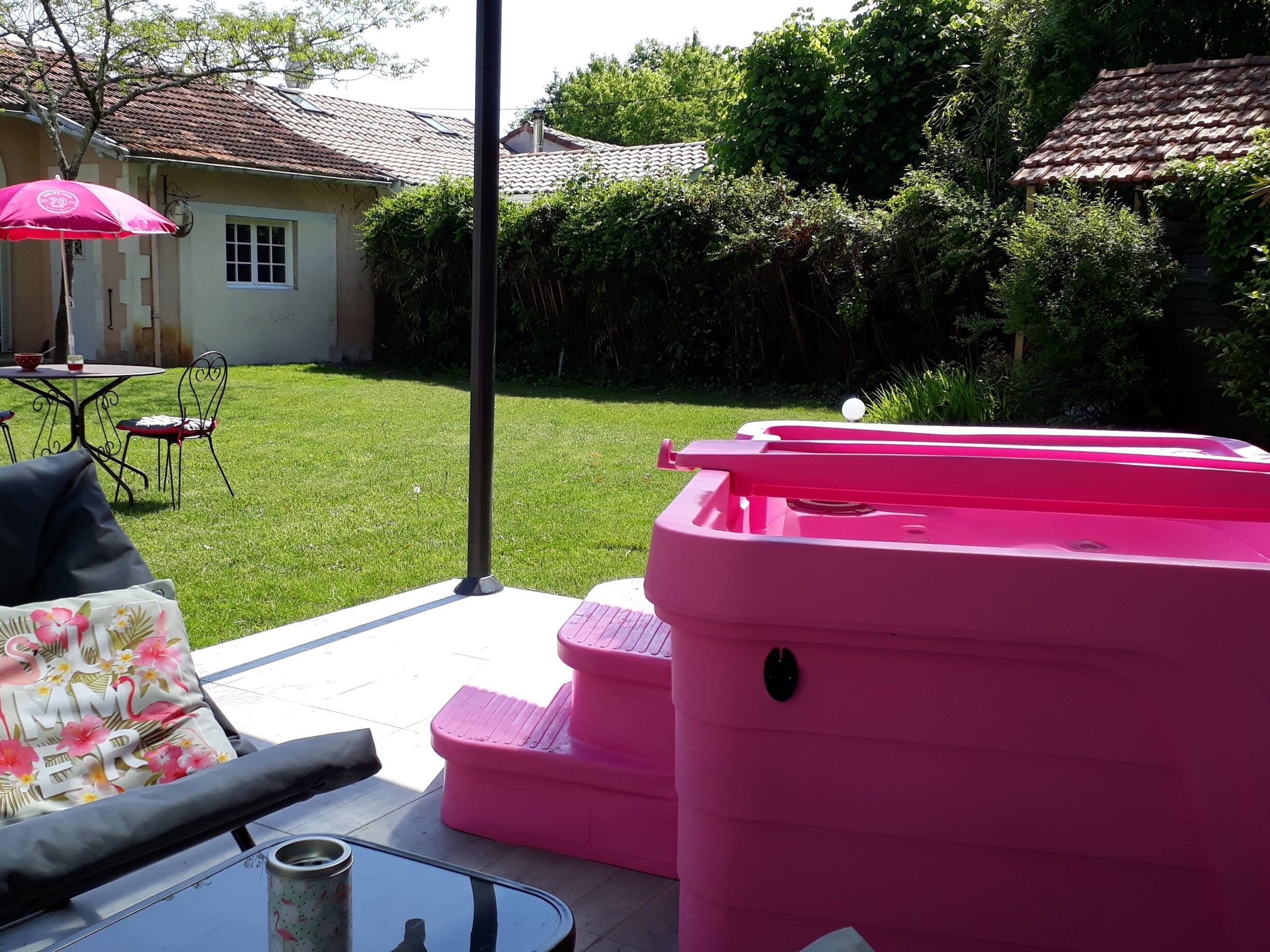 Un cortile con patio, una vasca idromassaggio rosa e un tavolo da pranzo con sedie.