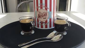 Two shot glasses of dark liquid, a vintage sugar canister, and a spoon on a black tray.