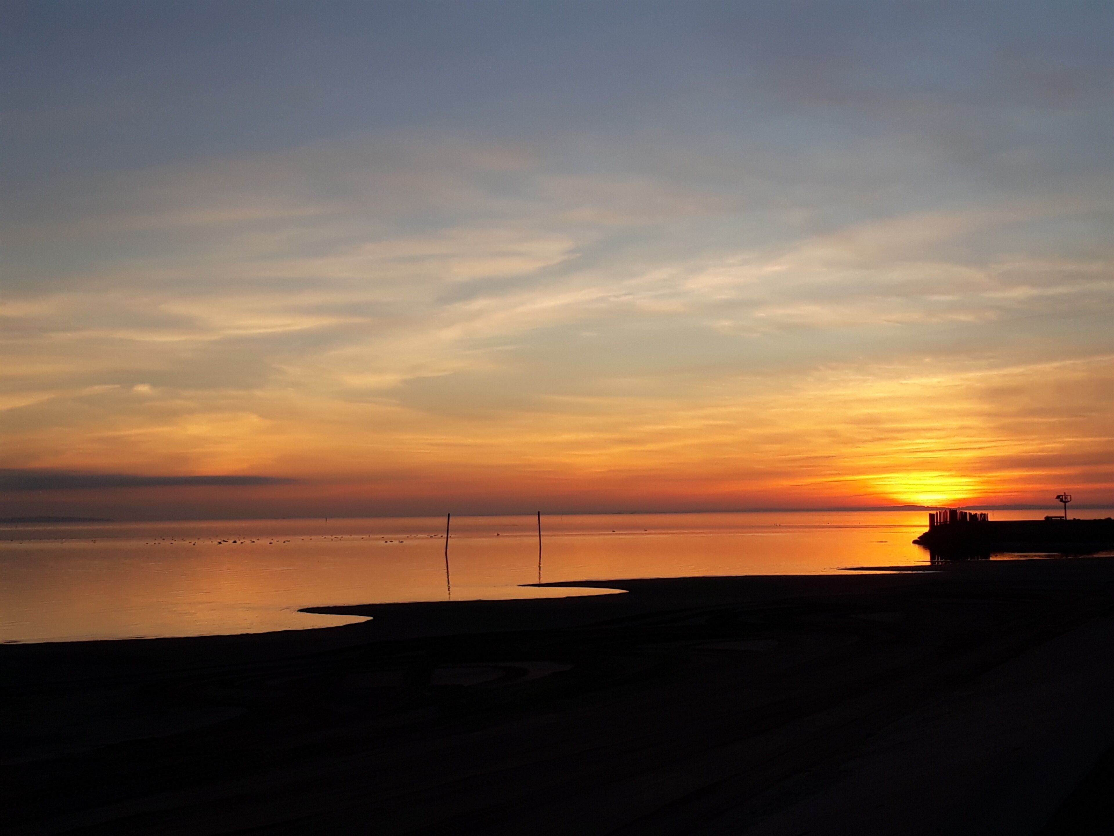Un atardecer sobre una masa de agua tranquila con un muelle que se adentra en el agua.