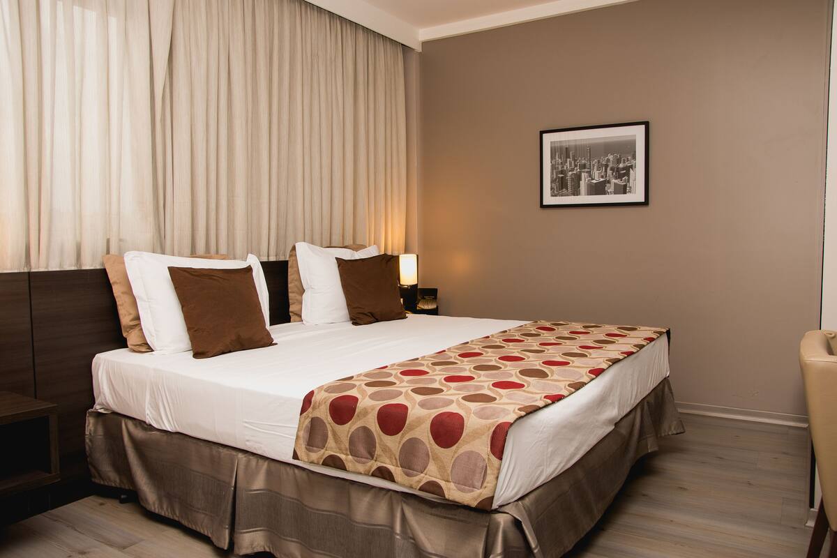 A hotel room with a large bed, a headboard, a bedside table, a lamp, and a framed picture on the wall.
