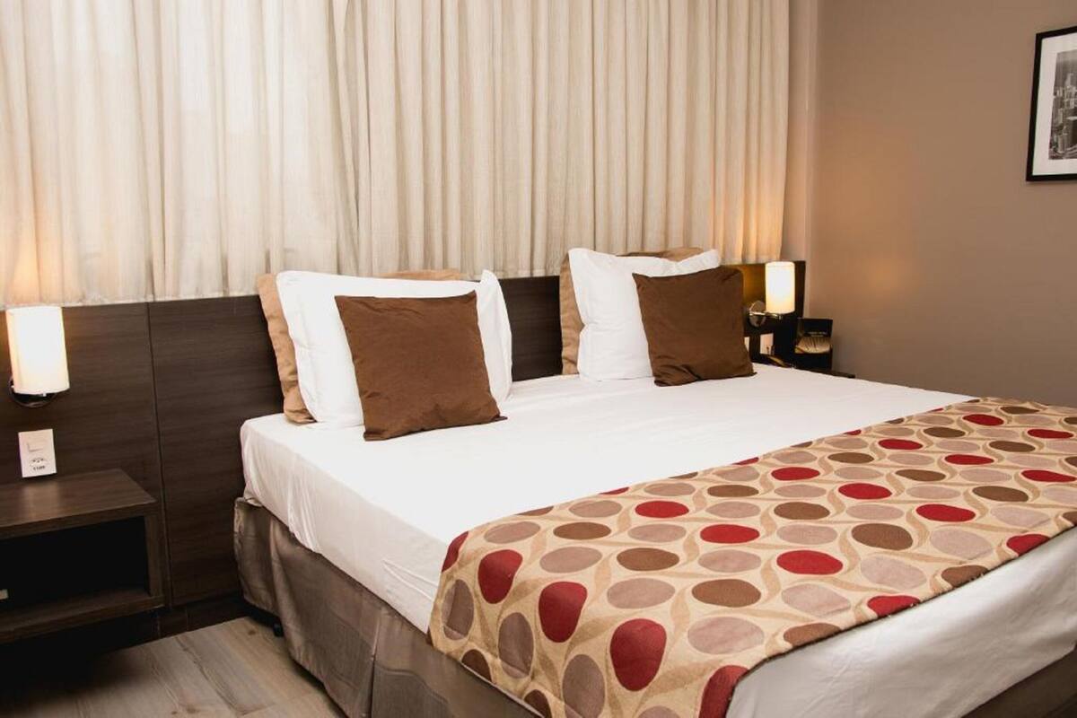 A hotel room with a large bed, two bedside tables, and a patterned throw blanket.