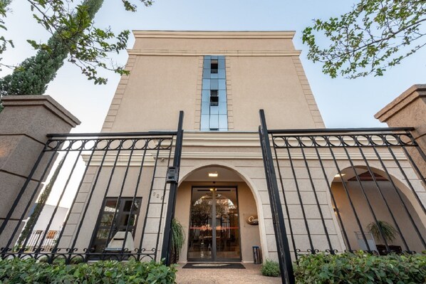 A hotel entrance with a beige facade, black metal gates, and a central arched doorway.