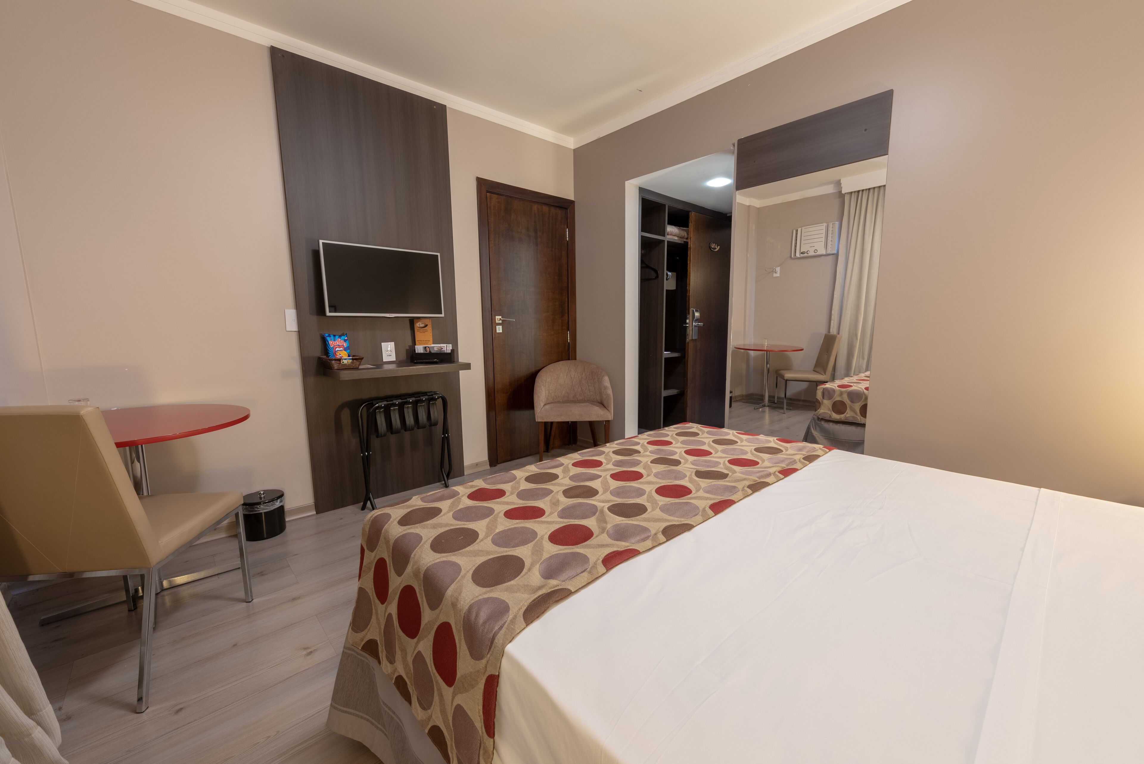 A hotel room with a bed, a desk with a chair, a TV, and a wardrobe.