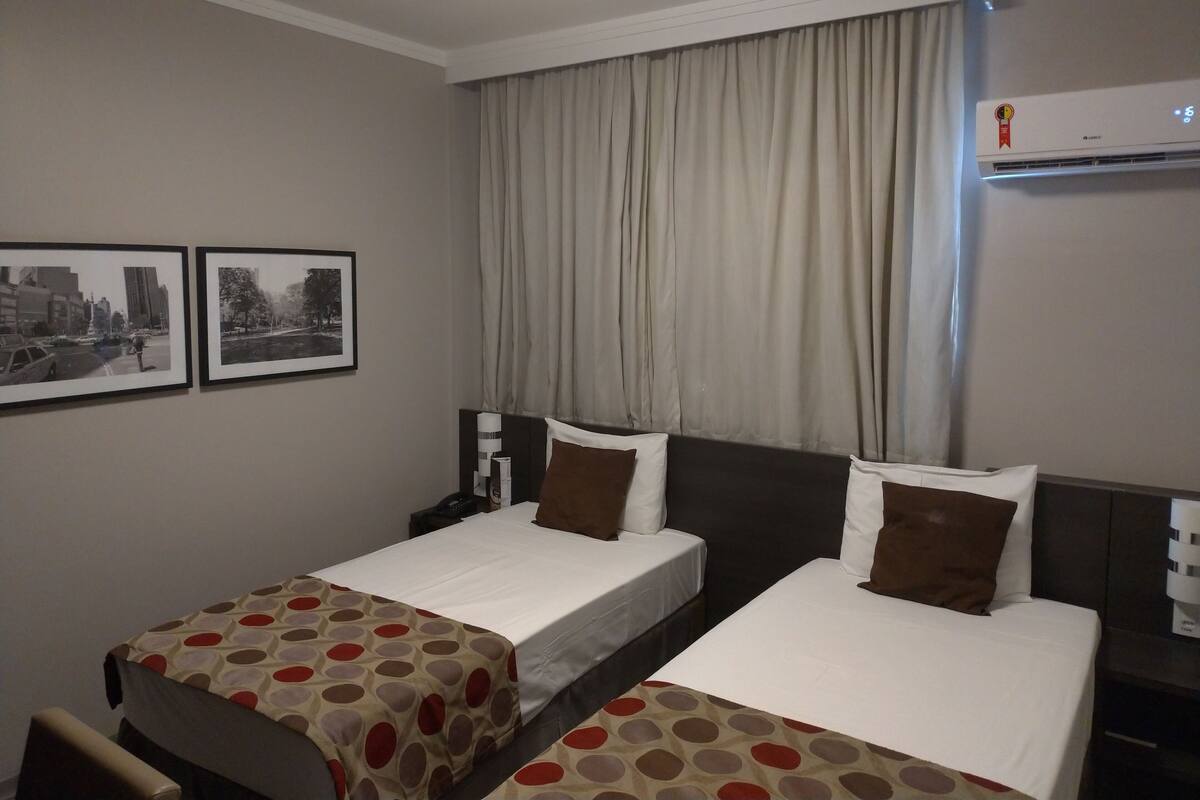 A hotel room with two beds, a desk, a chair, and two framed pictures on the wall.