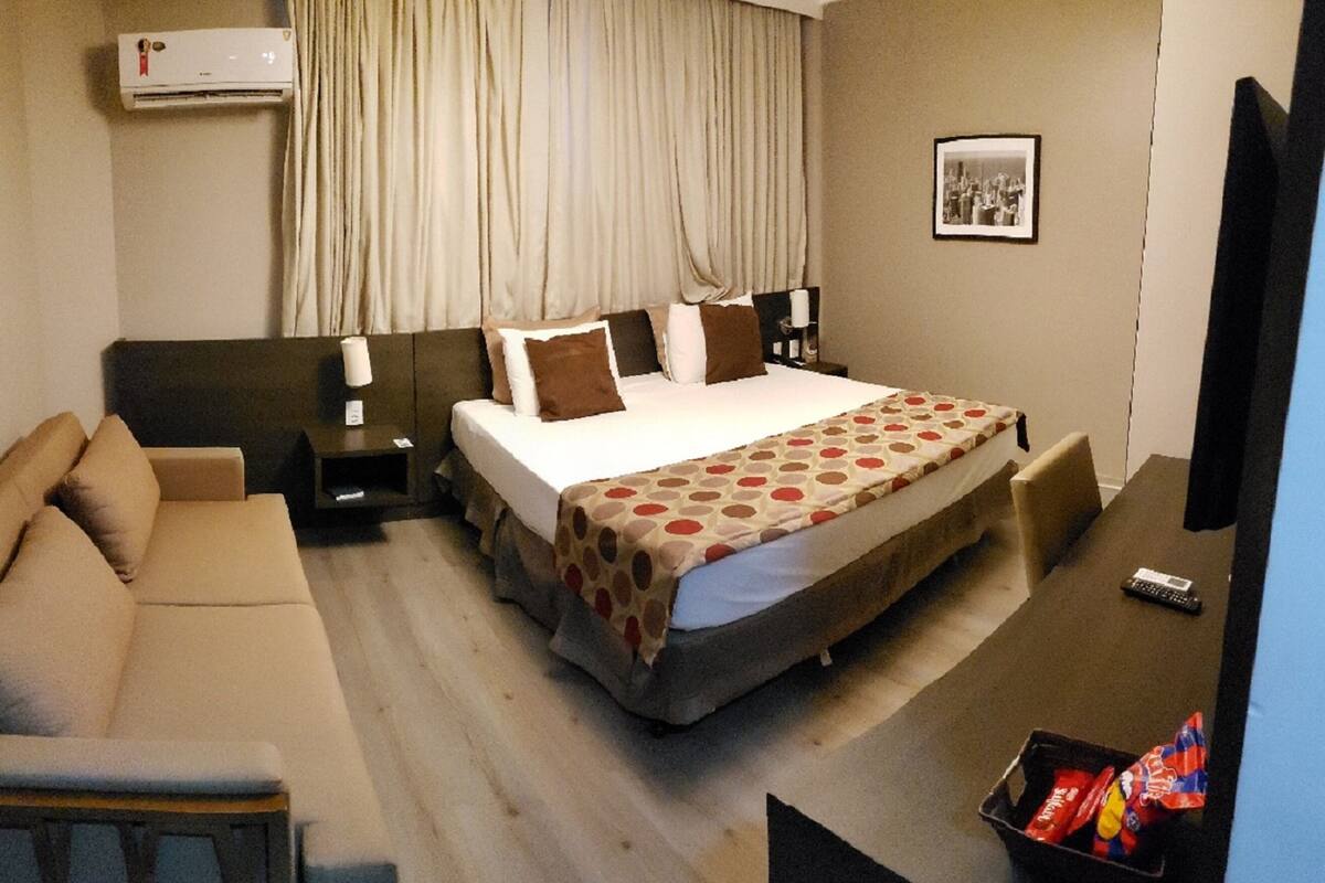 A hotel room with a bed, a sofa, a desk, and a TV.