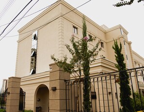 A beige building with a large arched entrance, a tall window, and a metal fence.