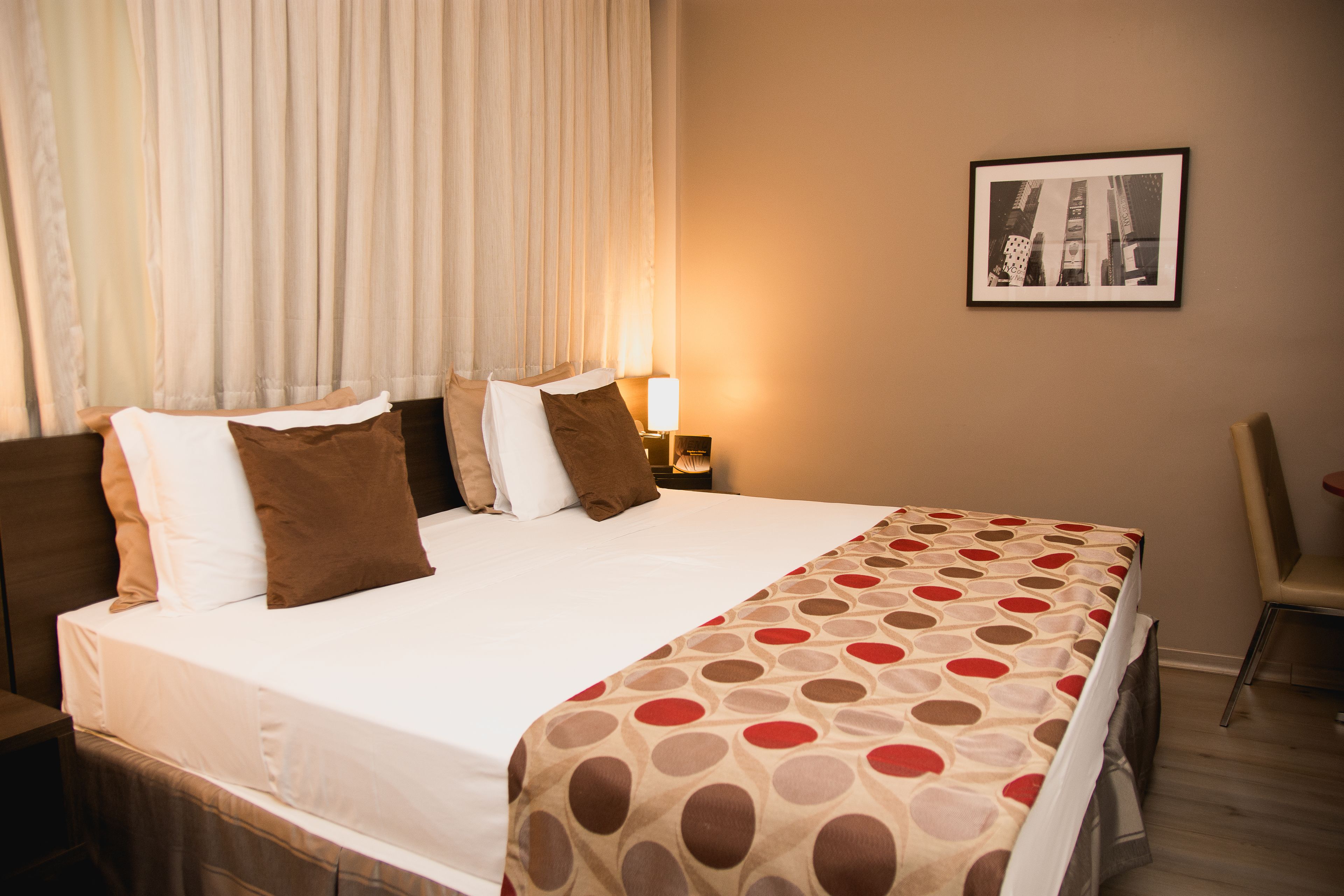 A neatly made bed with a patterned bedspread, a bedside lamp, and a framed picture on the wall.