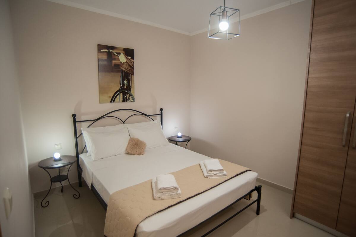A neatly made bed with a headboard, two bedside tables with lamps, a hanging light fixture, and a wardrobe.