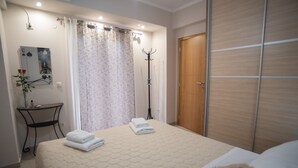 Un dormitorio ordenado con una cama, un perchero, un espejo y una puerta.