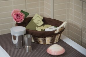 Un baño con una cesta de mimbre que contiene artículos de aseo, una taza de metal y una flor rosa.