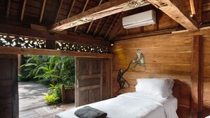 A wooden room with a bed, a wall-mounted air conditioner, and a door leading outside. - Villa Gambar (Kerobokan)