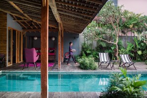 A pool area with a wooden pergola, lounge chairs, and lush greenery.