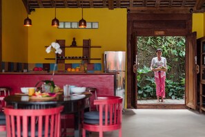 A kitchen with a yellow wall, a stainless steel refrigerator, and a dining area with red chairs and a table.
