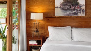 A wooden room with a bed, a nightstand with a lamp, a framed picture on the wall, and a window with curtains. - Villa Madah (Kerobokan)